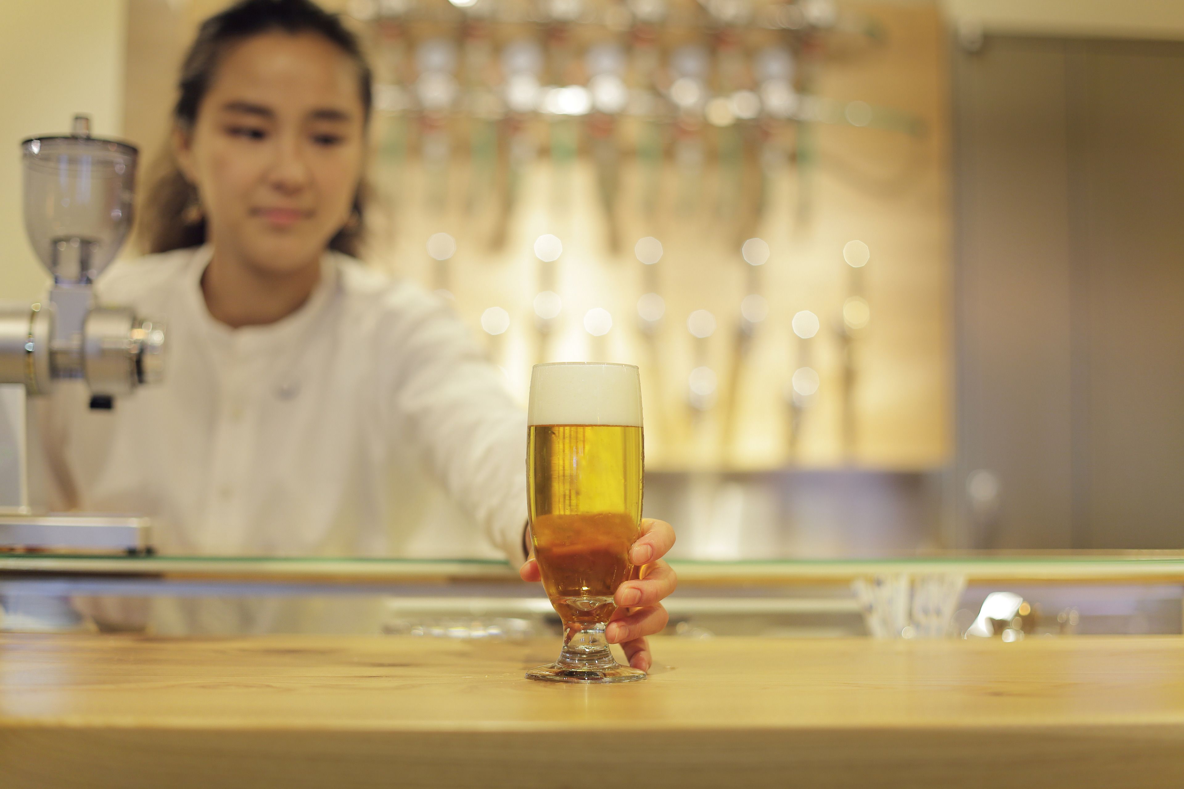 A person holding a glass of beer at a bar with a tap in the background.