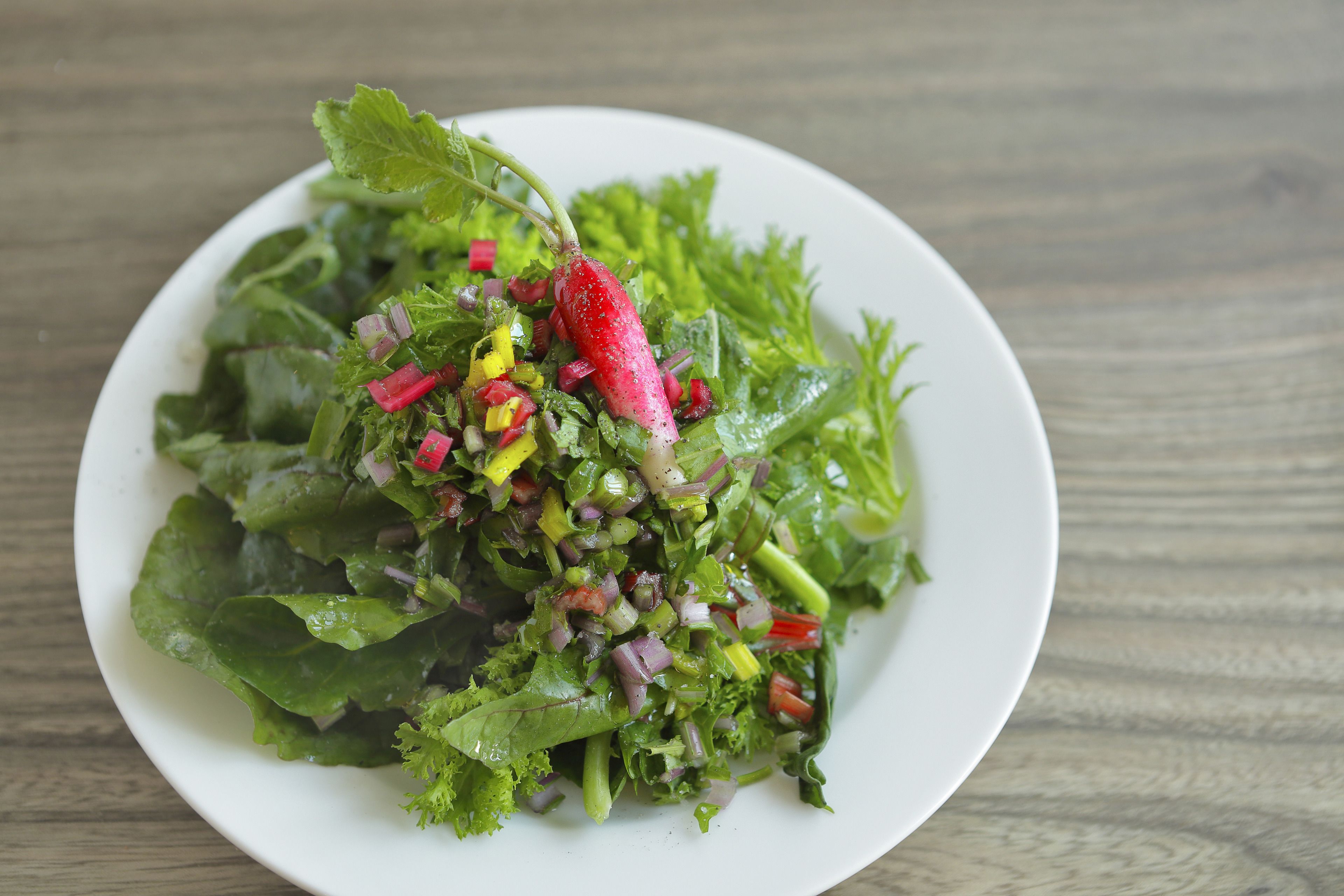 A white plate with a salad on a wooden table.