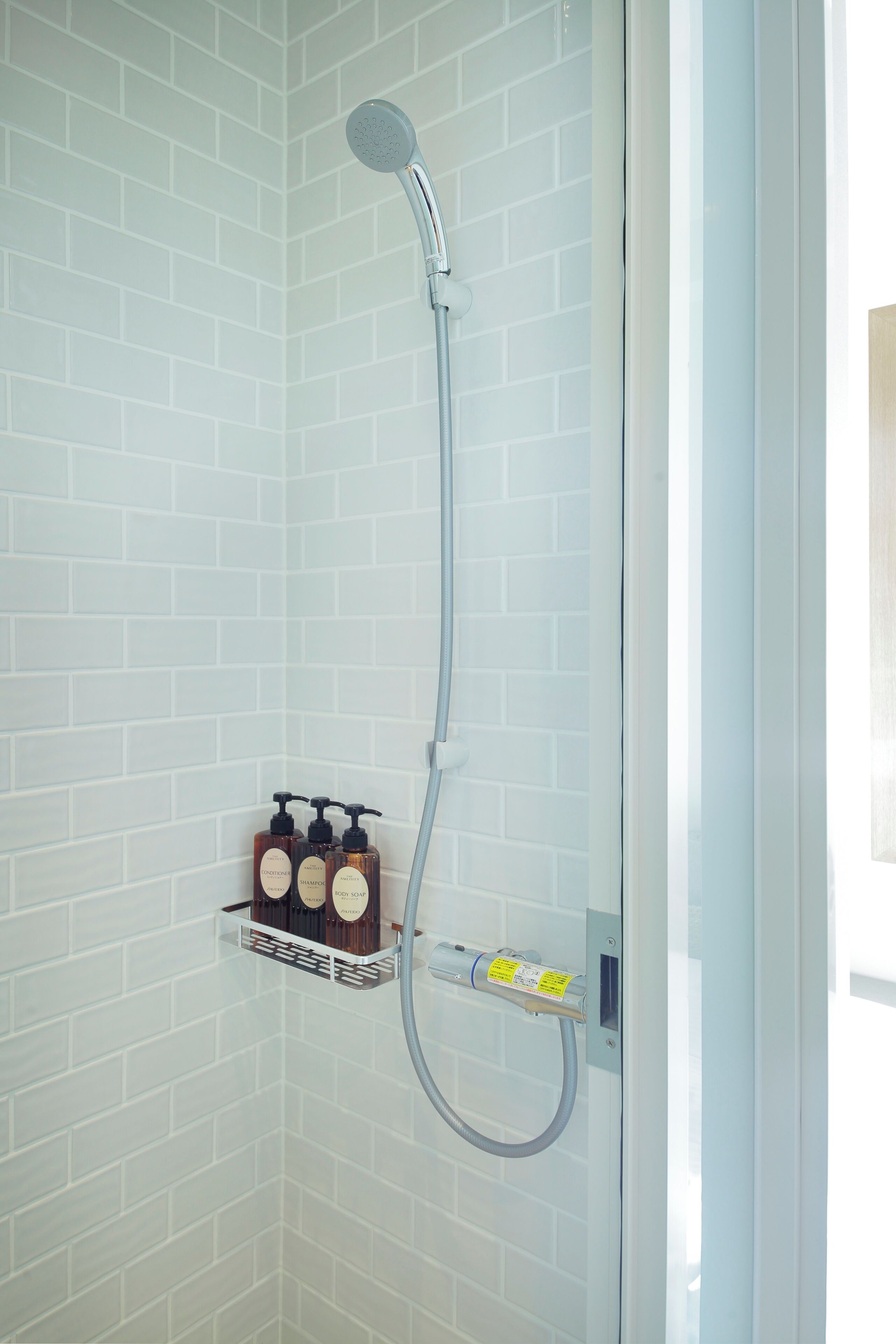 A shower with a handheld showerhead, a soap dispenser, and a small shelf with toiletries.