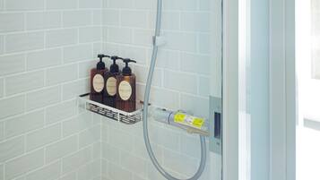 A shower with a handheld showerhead, a soap dispenser, and a small shelf with toiletries.