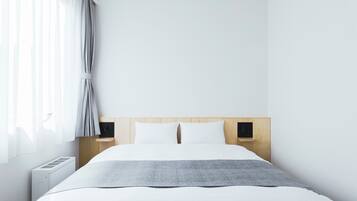 A minimalist hotel room with a large bed, a bedside table, a nightstand, and a window with curtains.