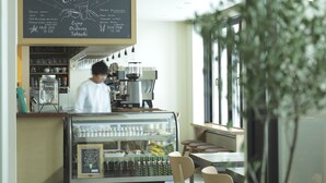 A coffee shop with a chalkboard menu, a coffee machine, and a display case with bottled drinks. - HOTEL NUPKA (Obihiro)