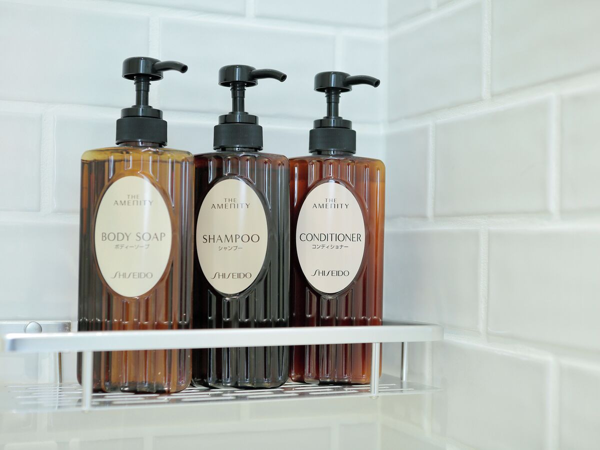 Tres botellas de jabón corporal, champú y acondicionador de The Amenity sobre una estantería blanca.