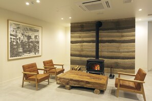 A cozy living room with a large fireplace, wooden furniture, and a cityscape painting on the wall. - HOTEL NUPKA (Obihiro)