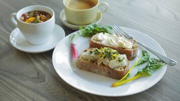 A plate with two slices of bread topped with a white spread and greens, a cup of tea, and a small bowl of soup.