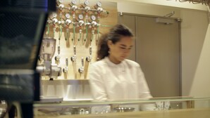 A person in a white chef's coat standing in a kitchen with stainless steel appliances and a glass counter. - HOTEL NUPKA (Obihiro)