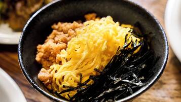 A bowl of food with noodles, a yellowish substance, and seaweed on a wooden table.