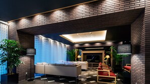 A modern lobby with a brick wall, a sofa, a red chair, and a floor lamp.