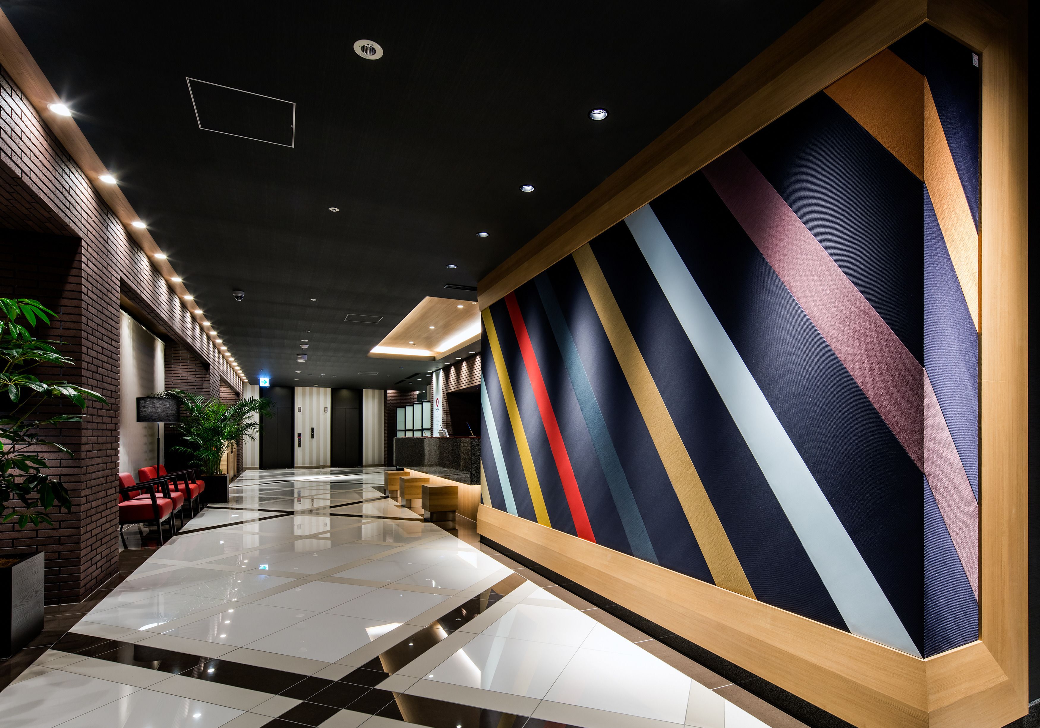A modern hotel lobby with a long reception desk, seating area, and a large wall with a geometric pattern.