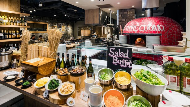 A buffet area with various food options and a pizza oven in the background.