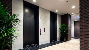 A modern elevator area with black and white walls, a wooden floor, and potted plants.