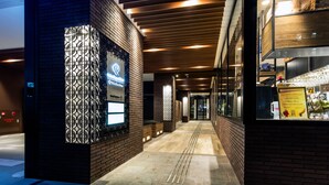 A modern hotel entrance with a brick facade, a reception area, and a glass door leading inside.