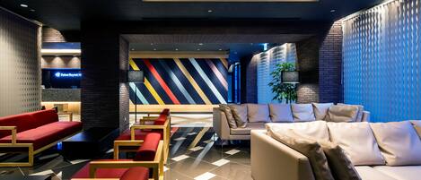 A modern lobby with a mix of seating areas, including red sofas and a beige sofa, and a patterned wall in the background.