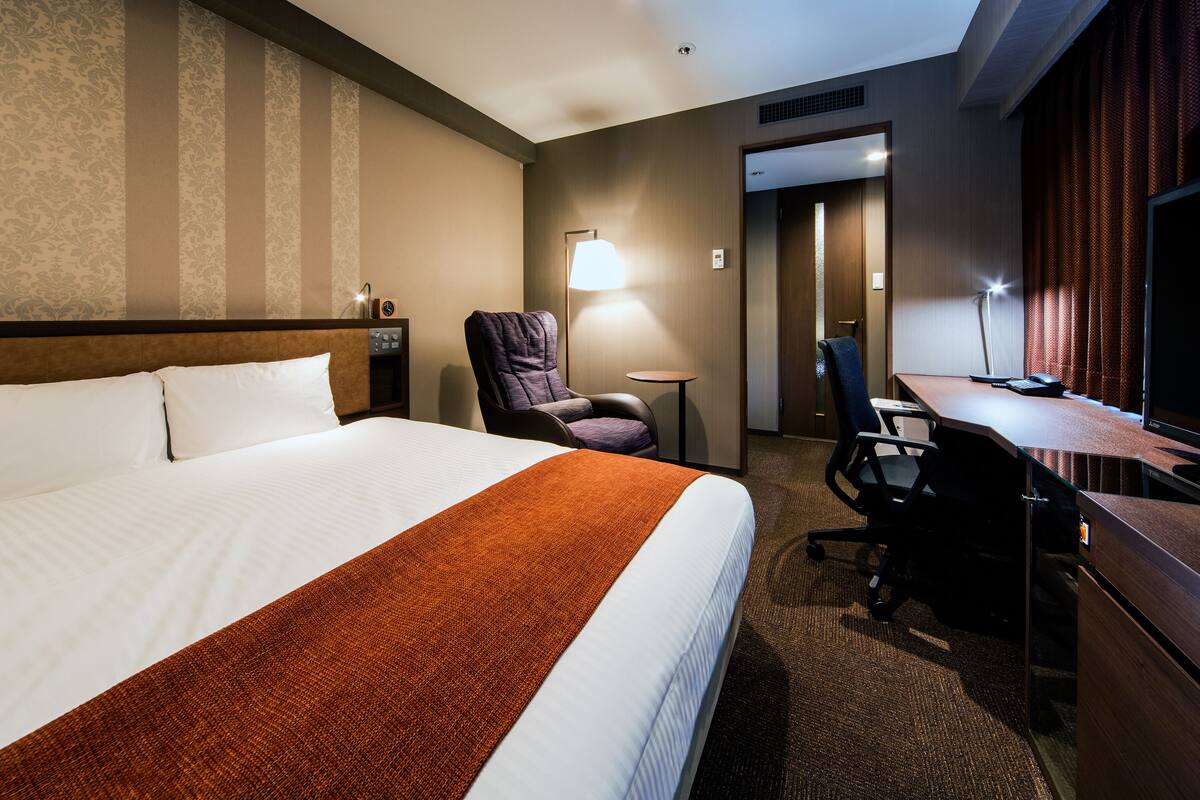 A hotel room with a large bed, a desk, a chair, a lamp, and a television.