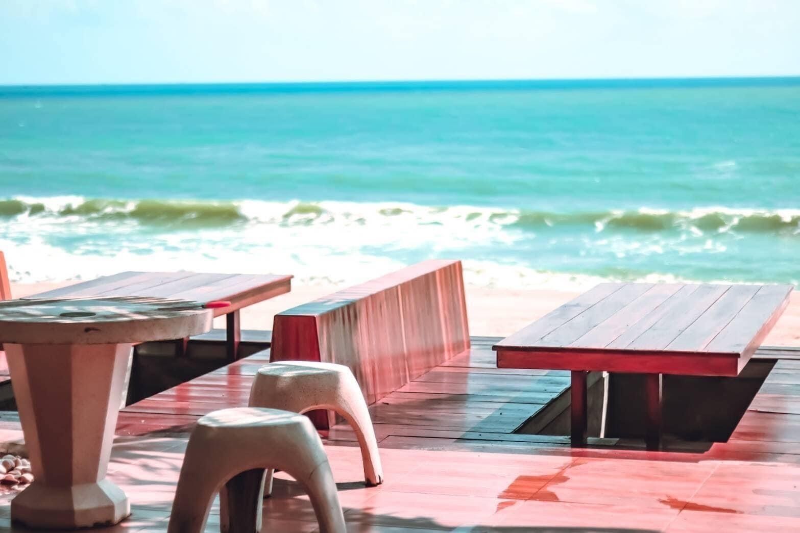 A beachside seating area with wooden tables and benches, overlooking the ocean.