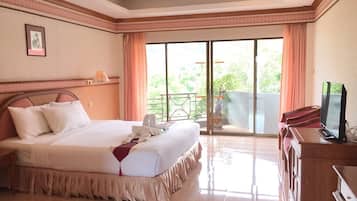 A hotel room with a large bed, a television, and a balcony with a view of greenery.