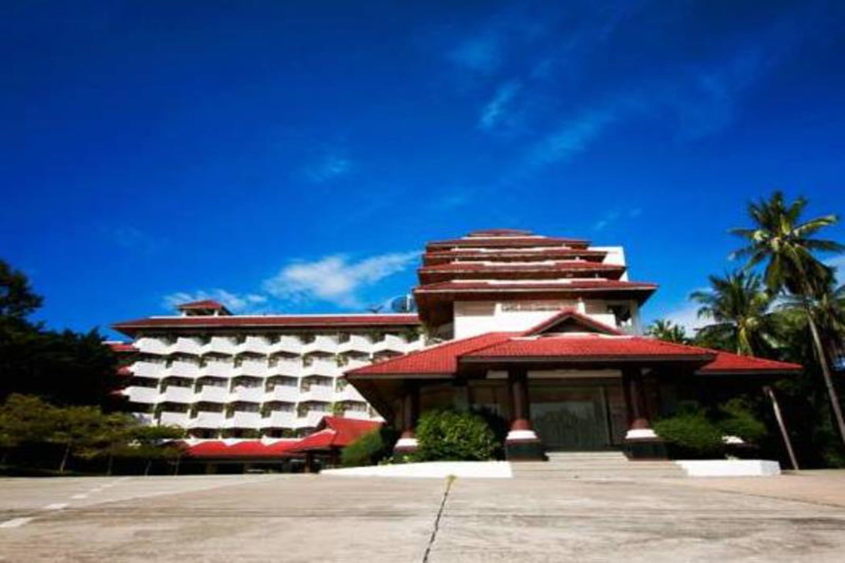 A multi-story hotel with a red roof and white walls, featuring a central entrance and multiple balconies.