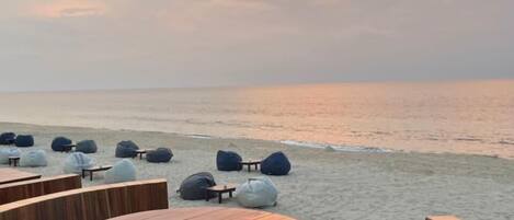 A beachside seating area with round wooden tables and bean bags.