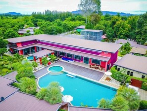 A modern building with a swimming pool, surrounded by lush greenery and a mountainous backdrop. - The Canal Garden Resort (Tha Yang)