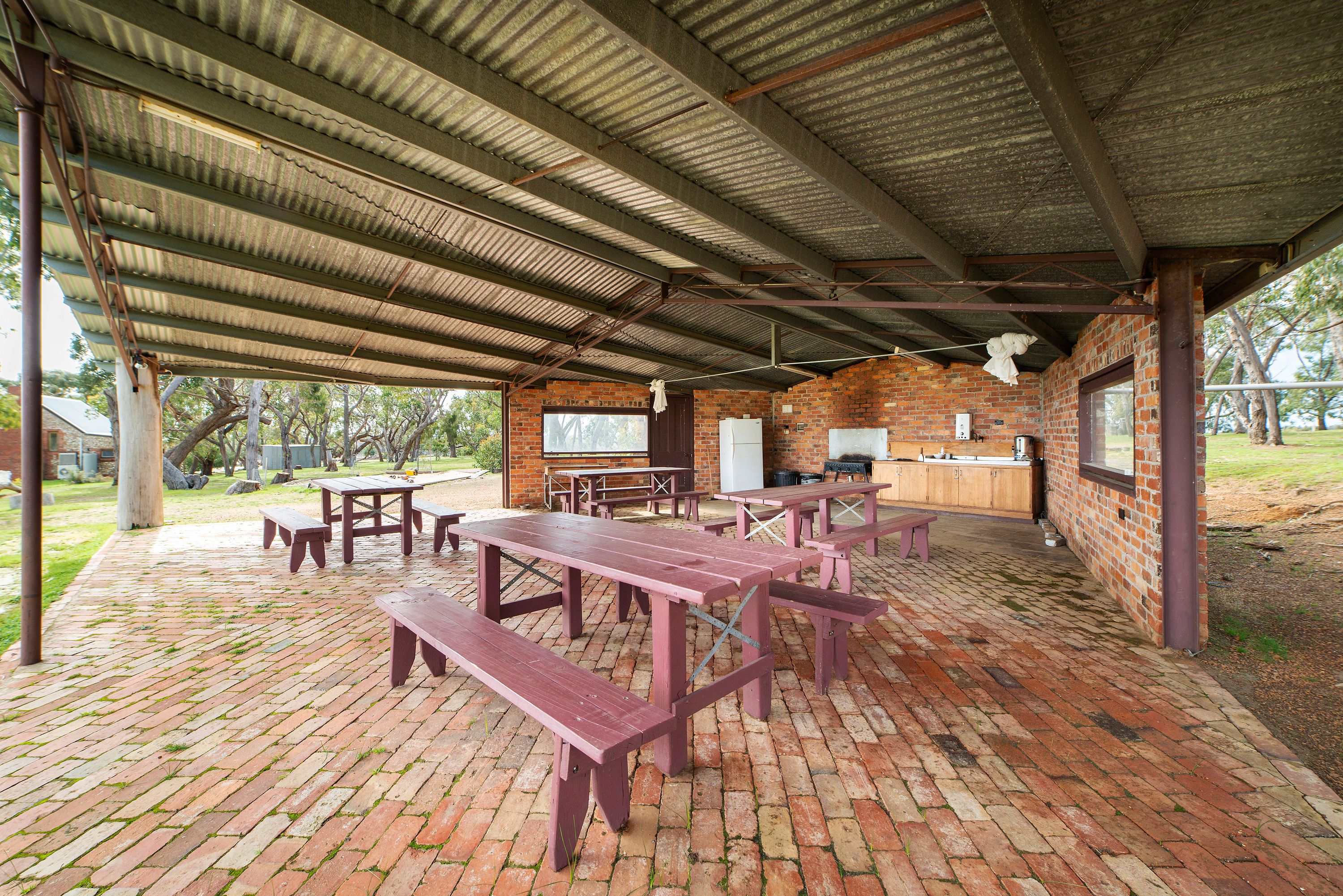 A covered picnic area with brick flooring and wooden picnic tables and benches.