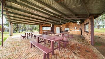 A covered picnic area with brick flooring and wooden picnic tables and benches.