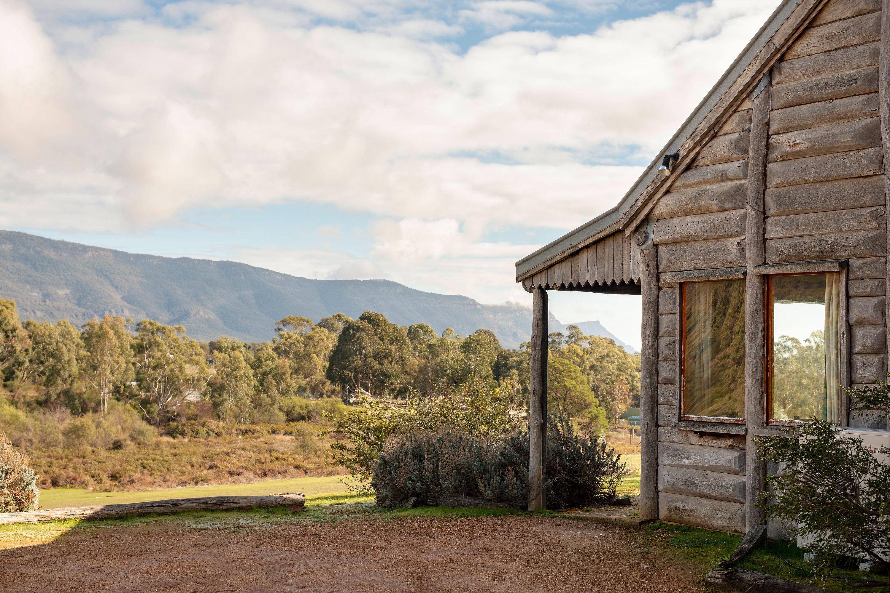 Un chalet rustique en bois, doté d’un porche couvert, niché au cœur d’un paysage naturel avec des montagnes en toile de fond.