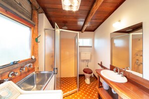 Ein Badezimmer mit Holzbalkendecke, Waschbecken, Toilette und Dusche.