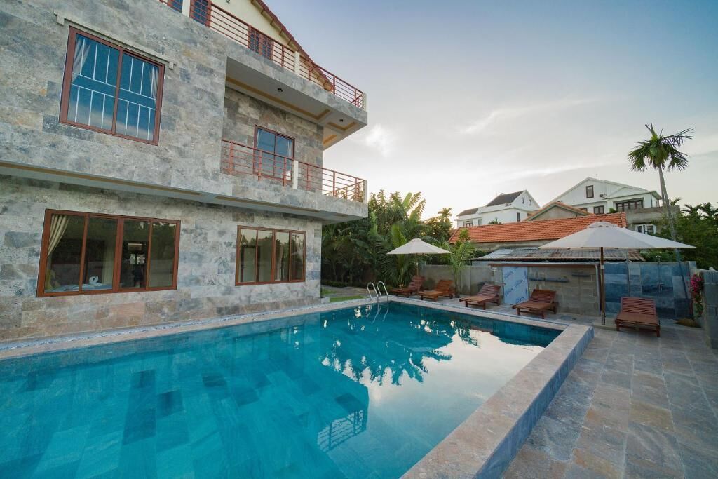 A two-story building with a swimming pool, outdoor seating, and a stone facade.