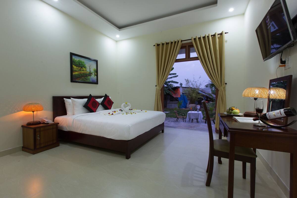 A hotel room with a bed, bedside lamp, TV, and a dining area with a table and chairs.