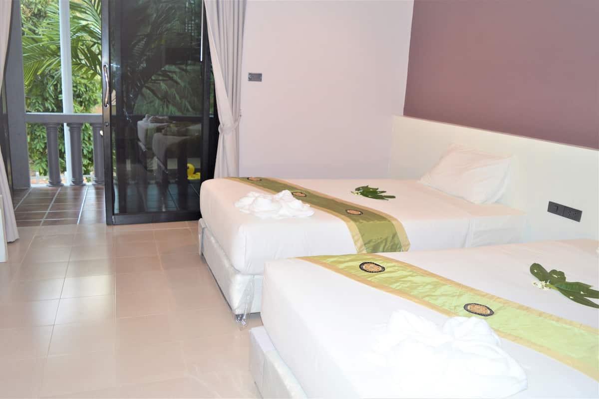 A hotel room with two beds, a sliding glass door leading to a balcony, and a view of greenery outside.