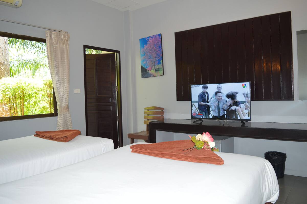 A hotel room with two beds, a TV, a painting, and a window with curtains.