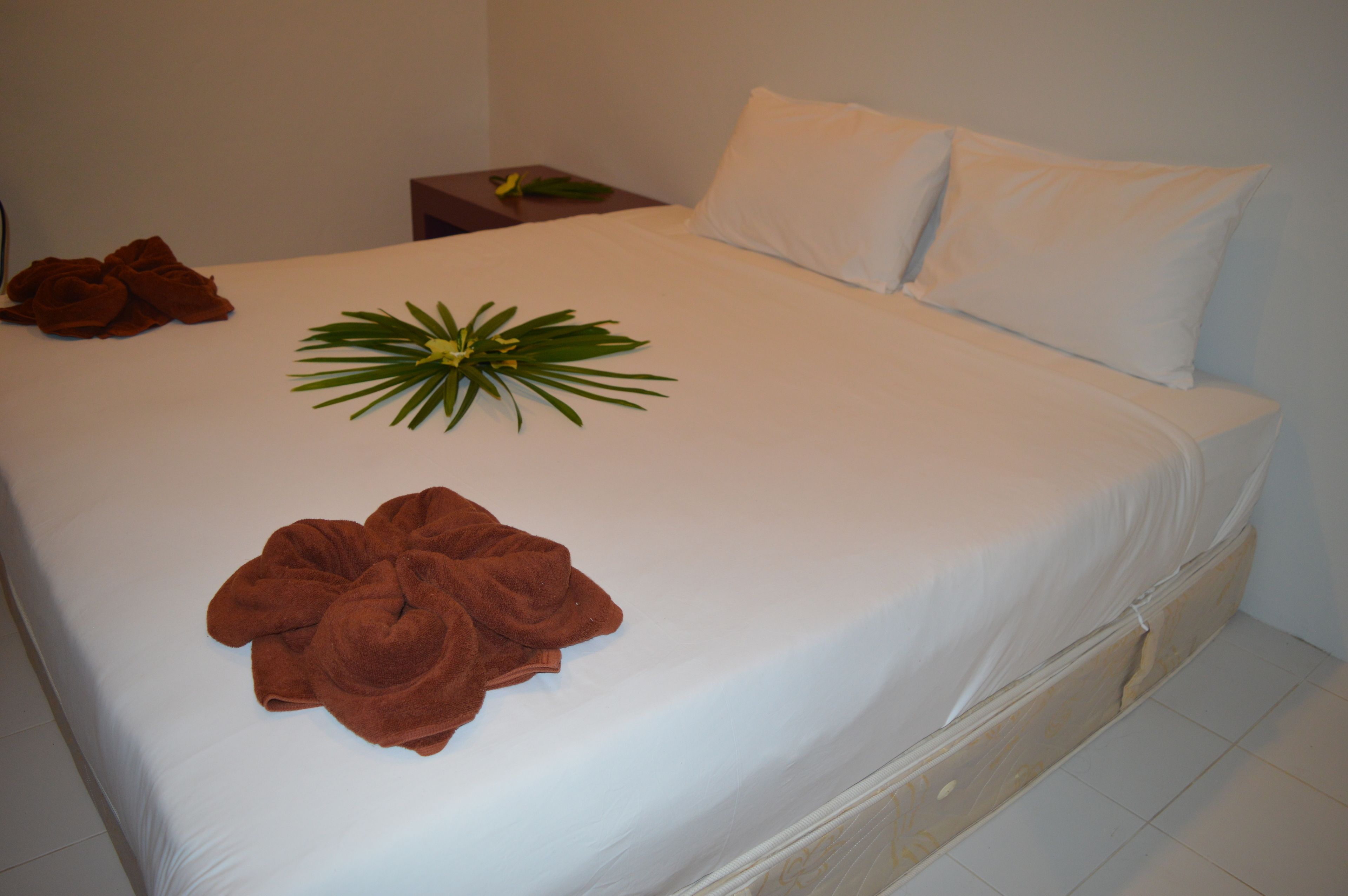 A neatly made bed with white linens, a brown towel, and a decorative plant.
