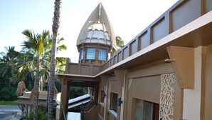 A modern building with a satellite dish, palm trees, and a statue. - B Square Hotel (Khanom)