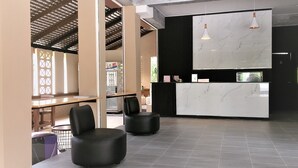 A modern reception area with a marble counter, black upholstered chairs, and a hanging pendant light. - B Square Hotel (Khanom)