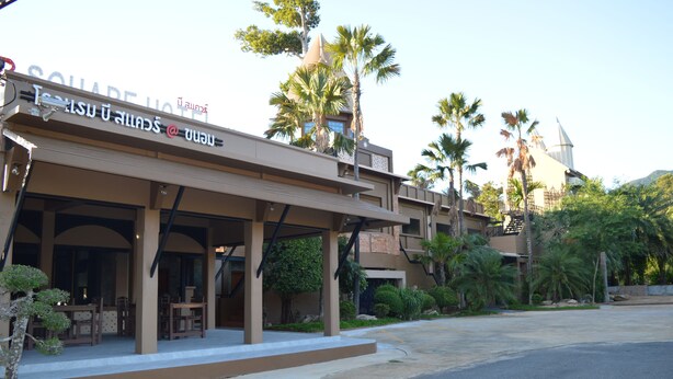 A hotel with a covered outdoor seating area, palm trees, and a clear sky. - B Square Hotel (Khanom)