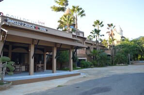 A hotel with a covered outdoor seating area, palm trees, and a clear sky.
