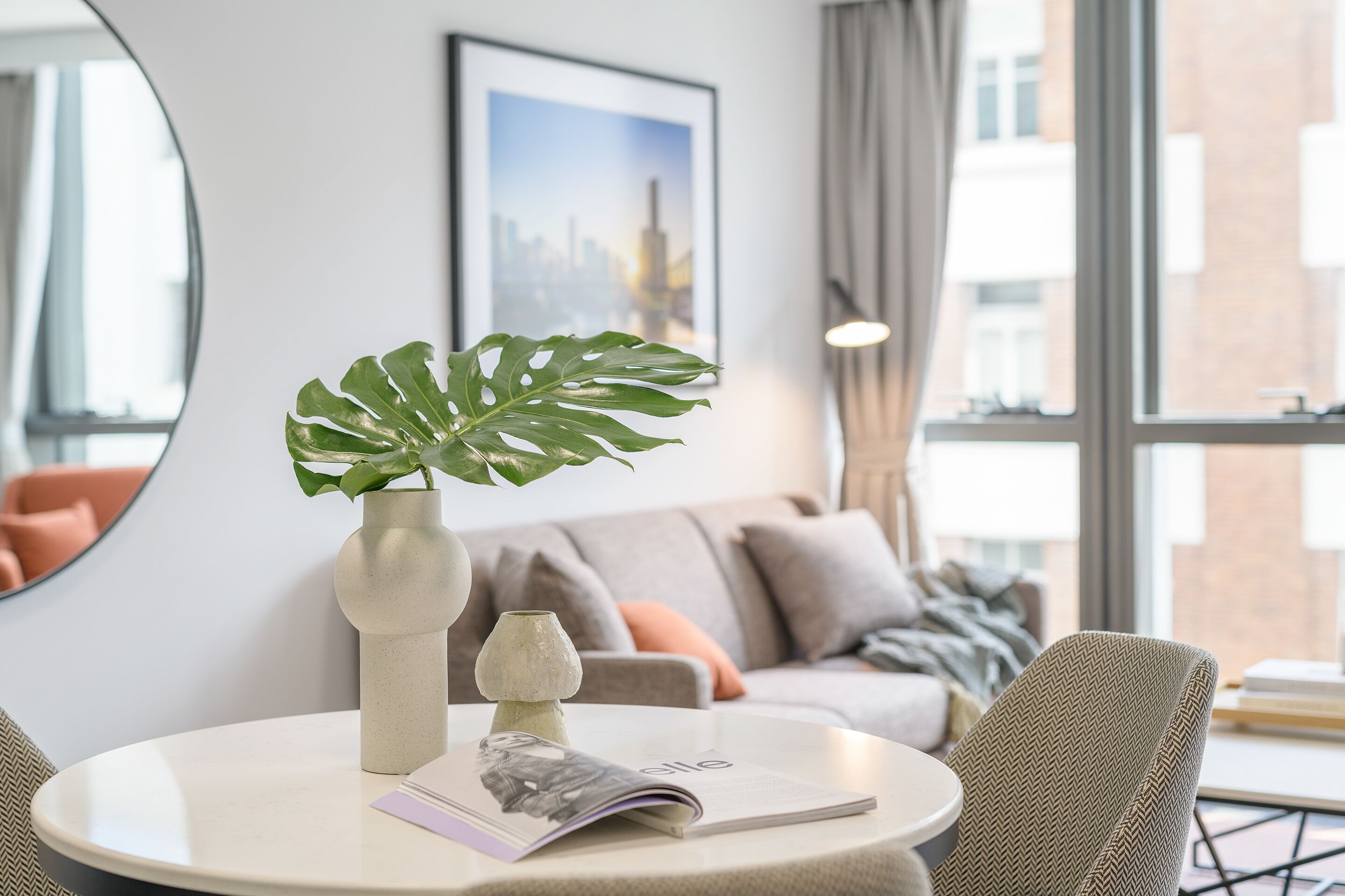 A modern living room with a round table, a potted plant, a magazine, and a sofa with cushions.