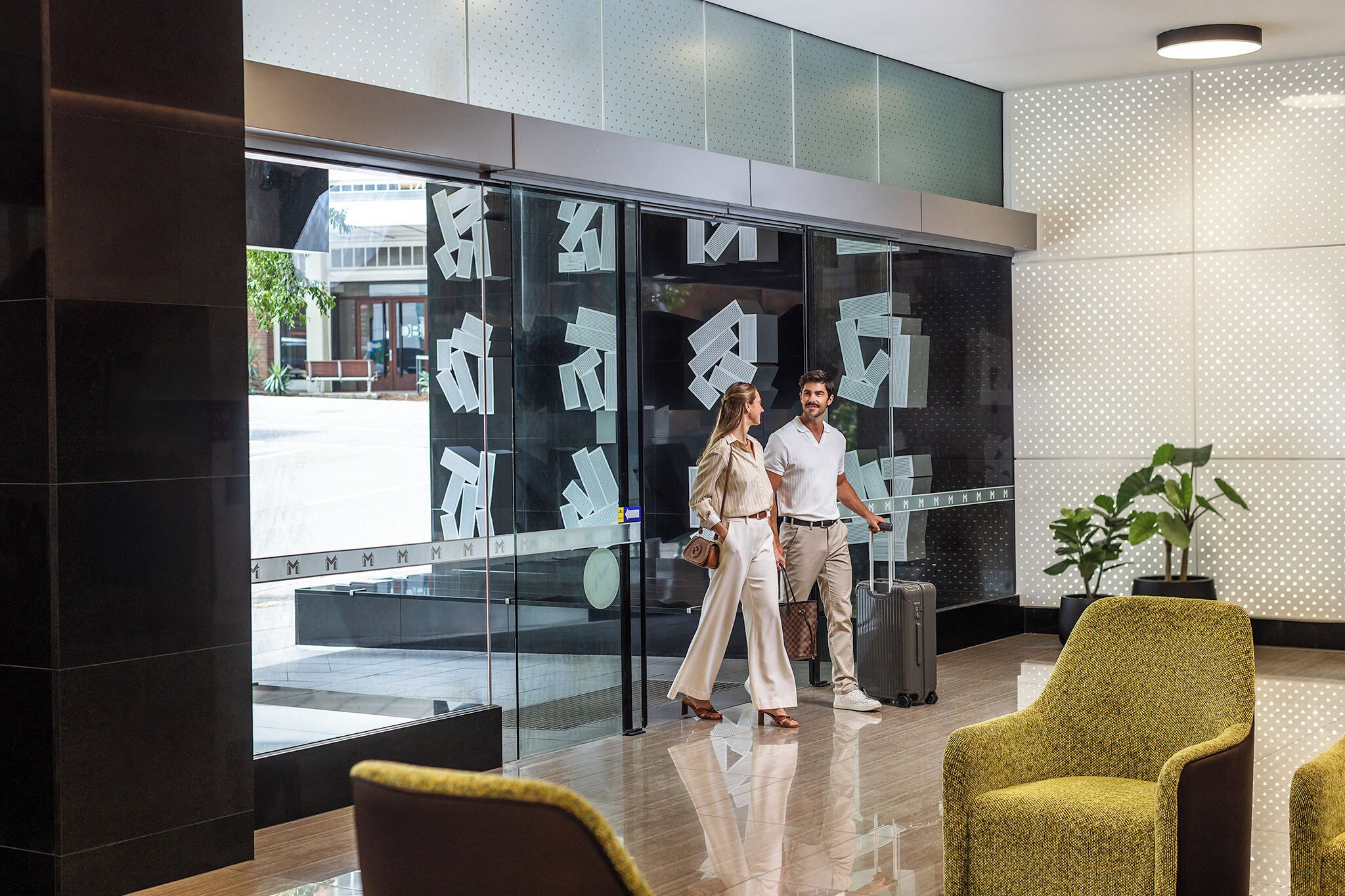 Un hall d’hôtel moderne avec un mur en verre, une plante en pot et un espace salon.