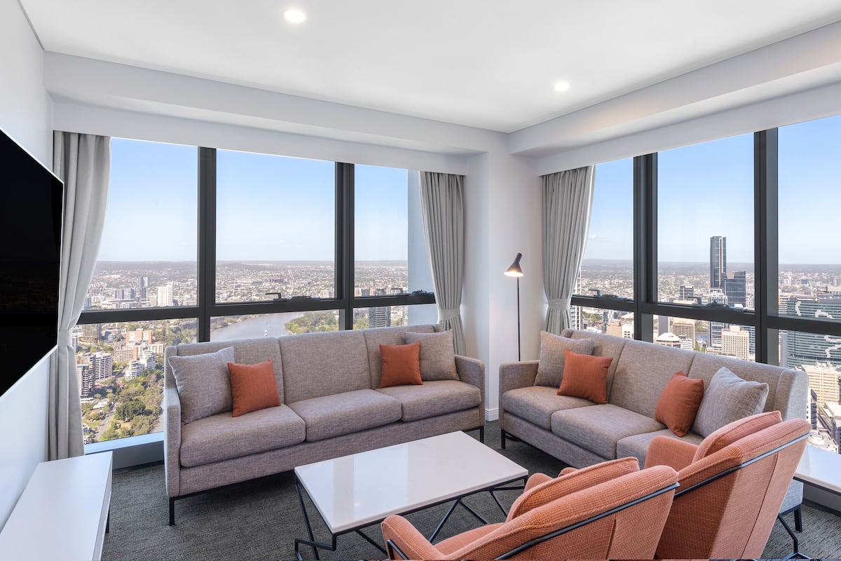Habitación de hotel moderna con un ventanal amplio que ofrece vistas a la ciudad, un conjunto de sofás y una mesita.