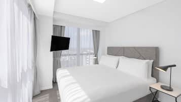 A modern hotel room with a large bed, a flat-screen TV mounted on the wall, and a bedside table with a lamp.