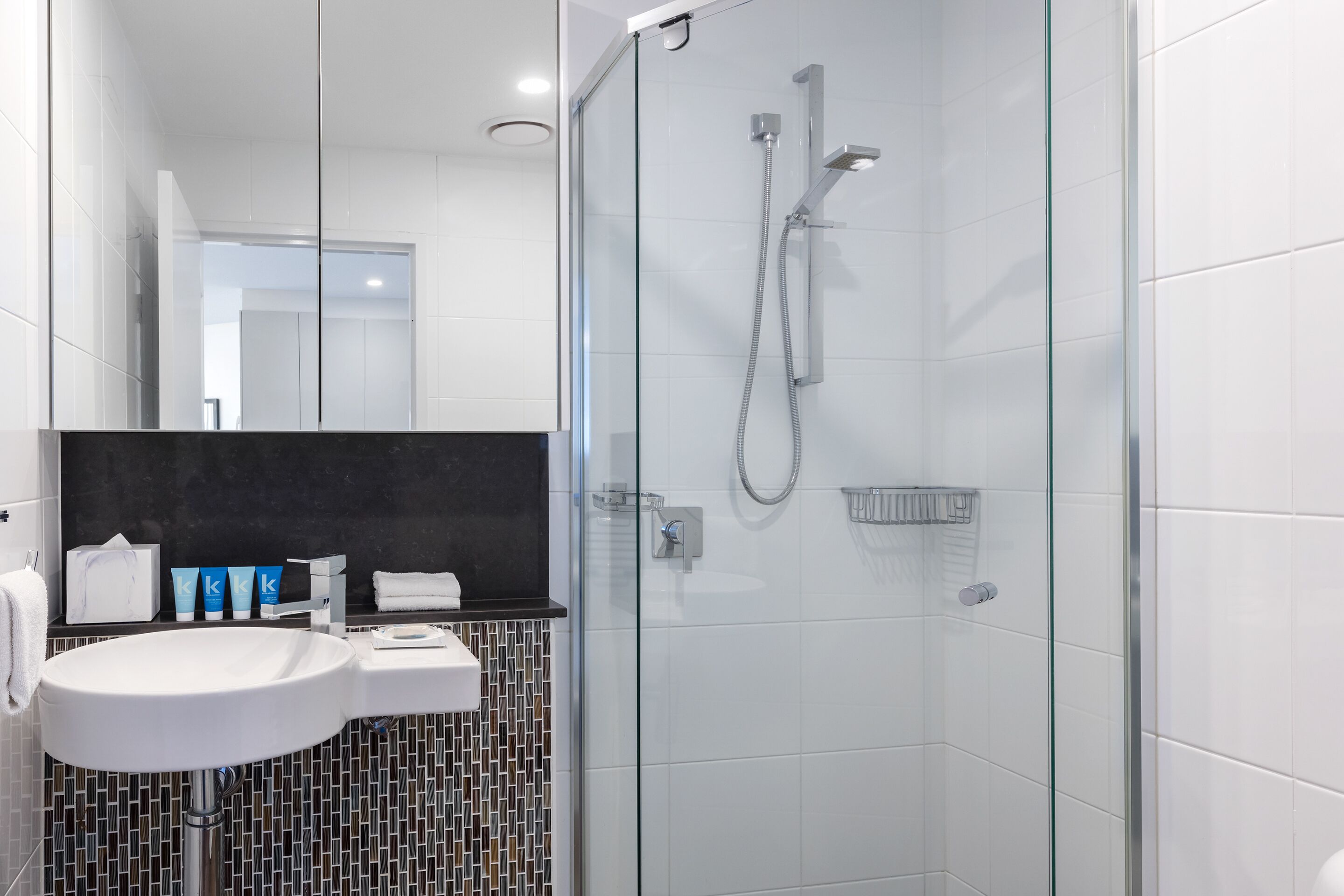A modern bathroom with a glass-enclosed shower, a white sink, and a tiled backsplash.