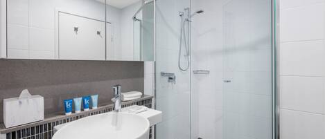 A modern bathroom with a glass-enclosed shower, a white sink with a marble countertop, and a mirror above the sink.