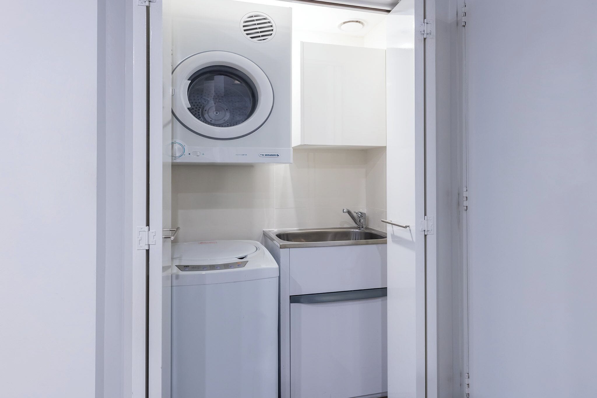 A compact laundry room with a washing machine, a dryer, and a sink.