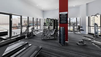 A modern gym with cardio machines, free weights, and a red pillar with gym rules.