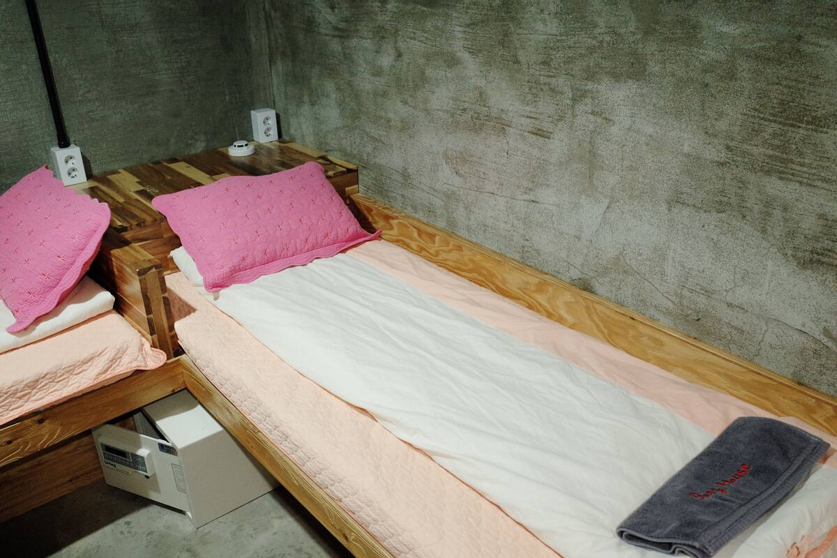 Un lit simple avec un cadre en bois, un matelas blanc et des oreillers roses.