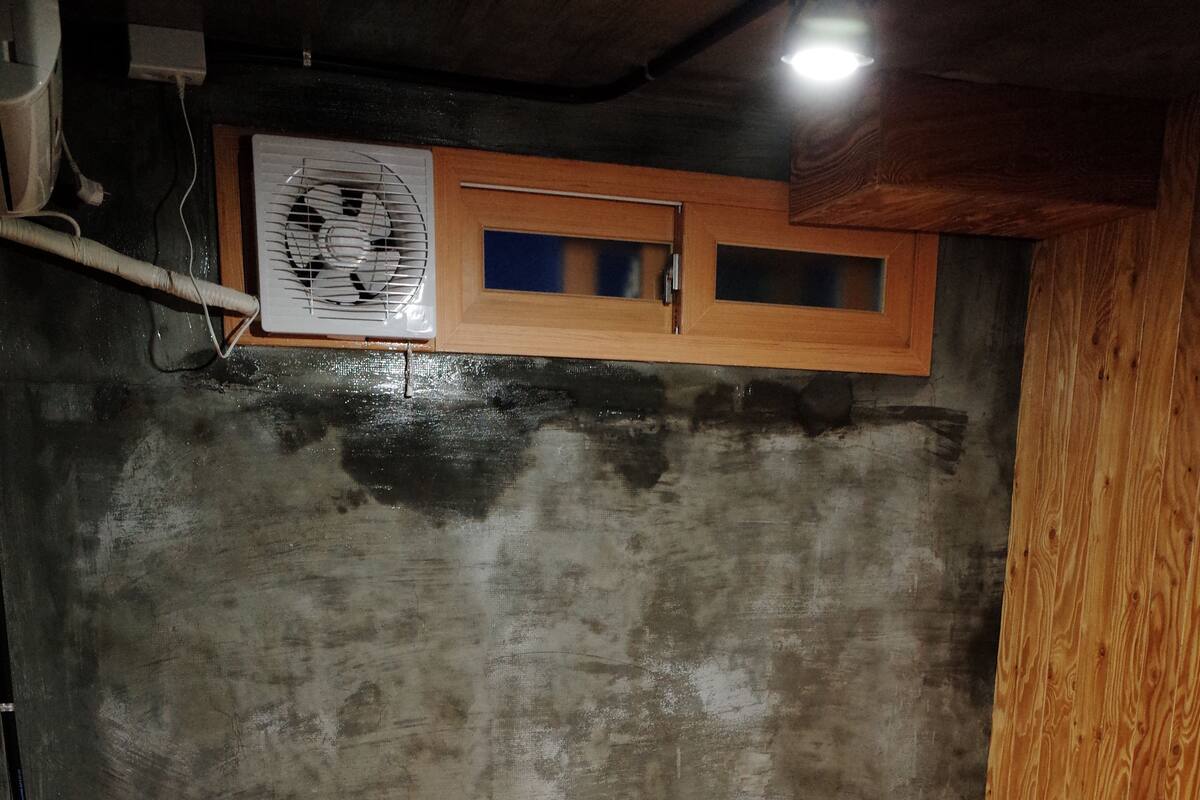 Une petite pièce agréable, dotée d’un lit simple, d’une tête de lit en bois, d’une petite fenêtre et d’un ventilateur fixé au mur.
