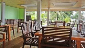 Un restaurante con mesas y sillas de madera, una pared verde y ventanas amplias con vistas a la vegetación.
