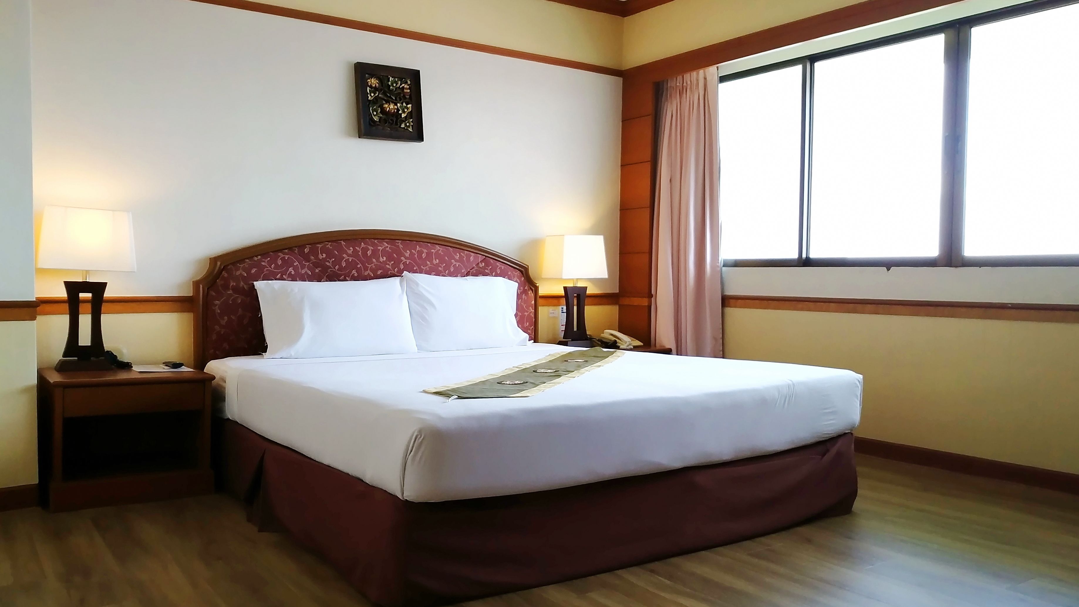A neatly made bed with white linens, two bedside tables with lamps, a telephone, and a window with curtains.