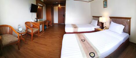 A hotel room with two beds, a desk with a chair, a television, and a small table with a kettle and cups.