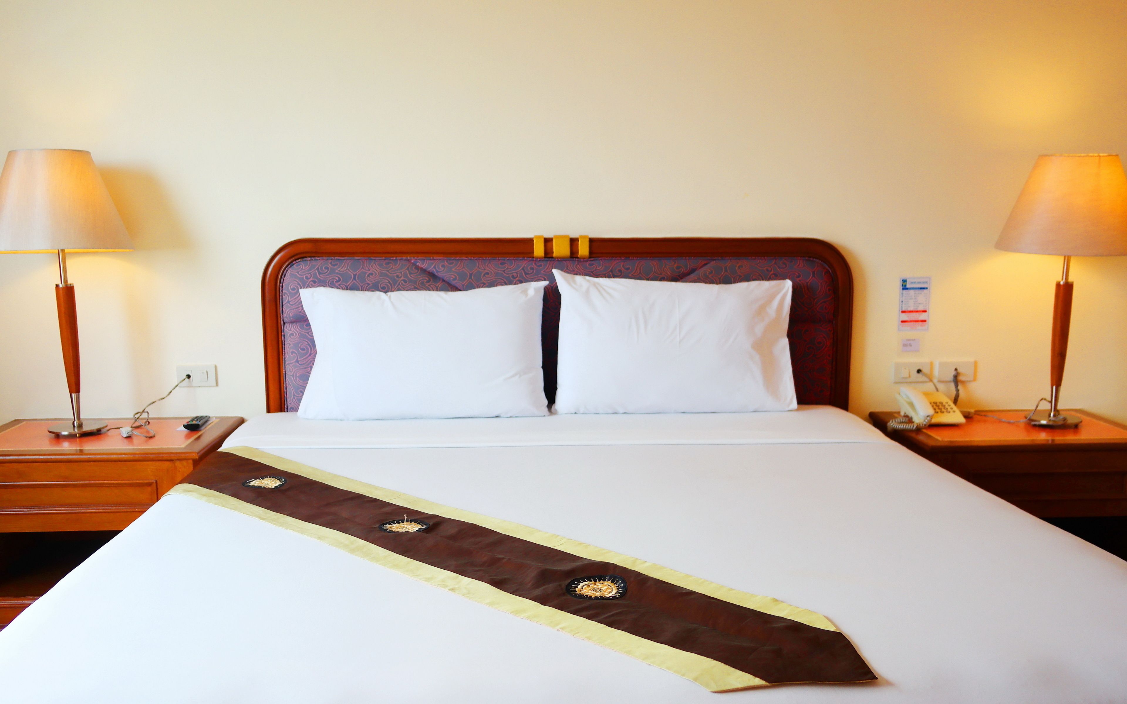 A hotel room with a neatly made bed, two bedside lamps, a telephone, and a small table with a lamp.